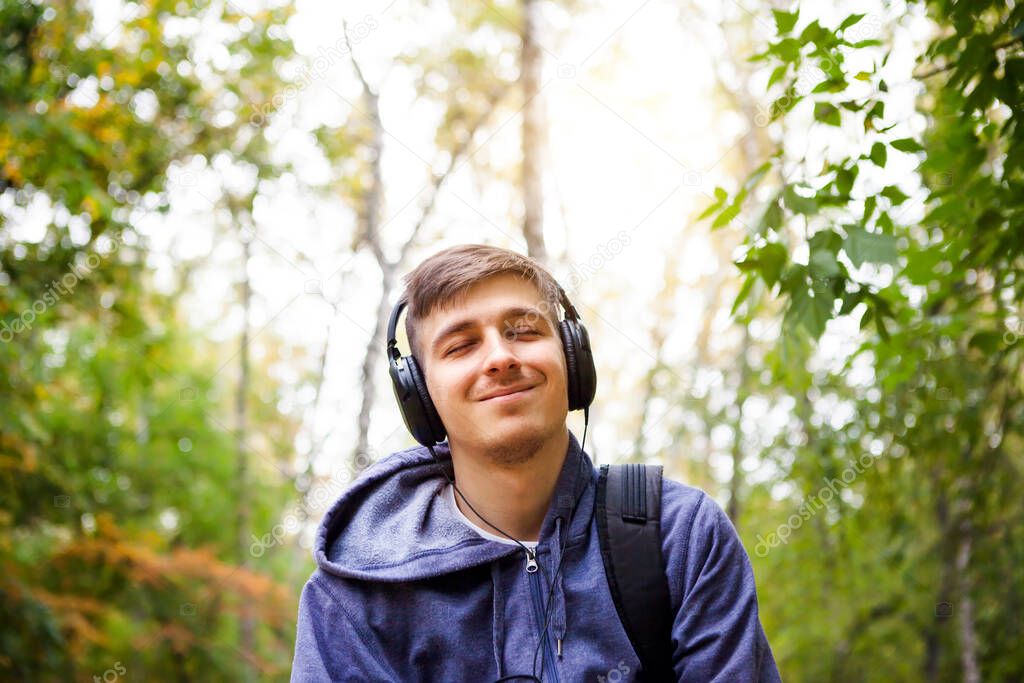 Happy Young Man in Headphones listen to the Music in the Forest