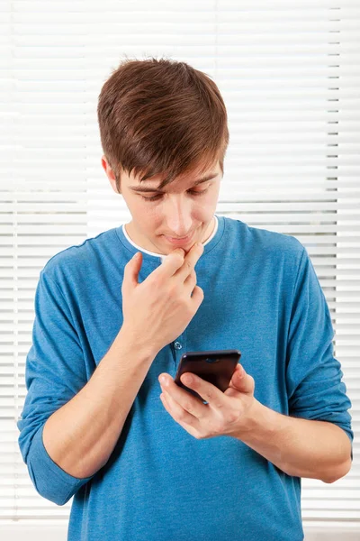 Orolig Ung Man Med Mobiltelefon Tänker Jalousie Bakgrund Ett Rum — Stockfoto