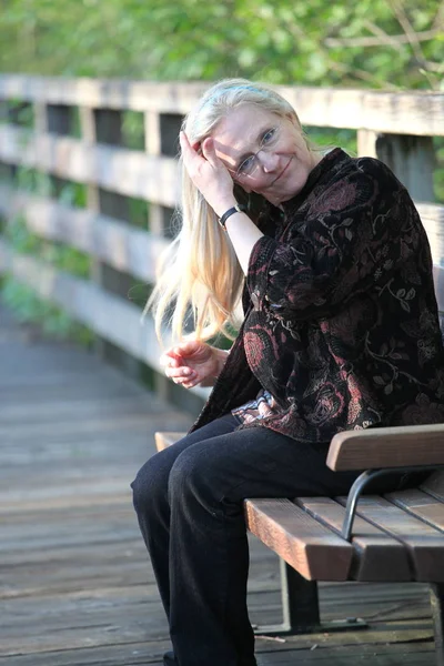 成熟した女性のブロンド美式屋外公園のベンチに座っています — ストック写真
