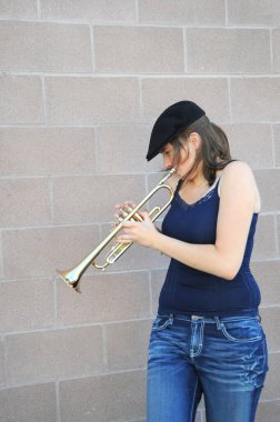 Dişi caz trompetçisi dışarıda duvara karşı kornasını çalıyor..