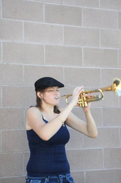 女性ジャズトランペット奏者は外の壁に対して彼女のホーンを吹いて — ストック写真