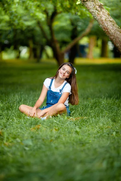 Schönes Teenie Mädchen Jeans Overalls Sitzt Auf Dem Gras — Stockfoto