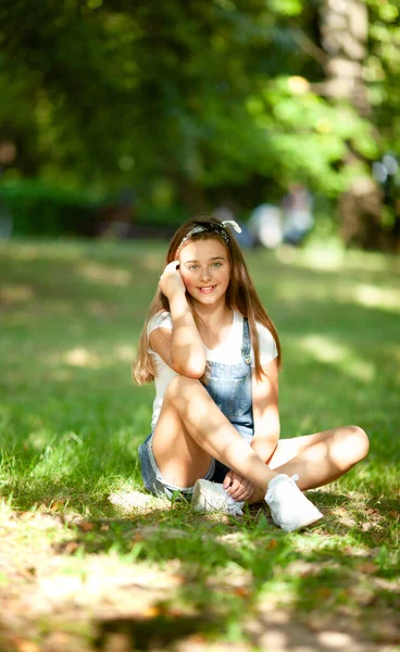 Schöne Teenager Mädchen Jeans Overalls Sitzt Auf Dem Gras Beleuchtet — Stockfoto