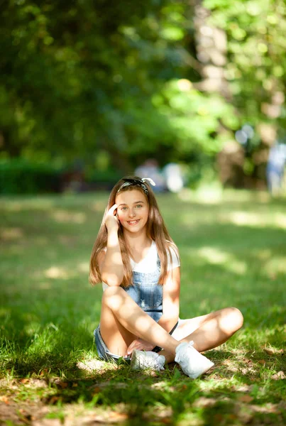 穿着粗斜纹棉布工作服的漂亮少女坐在草地上 阳光照射着她的小兔子 — 图库照片