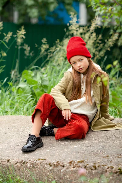 Sonbahar kıyafetleri içinde güzel bir kız beton bir blokta bacak bacak üstüne atmış oturuyor.