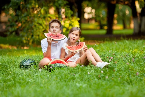 boy and girl sit on the grass and eat juicy watermelon