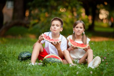 Oğlan ve kız çimenlerde oturur ve sulu karpuz yerler.