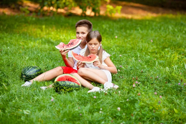 boy and girl sit on the grass and eat juicy watermelon
