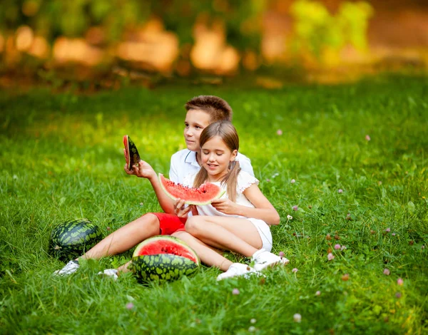 boy and girl sit on the grass and eat juicy watermelon