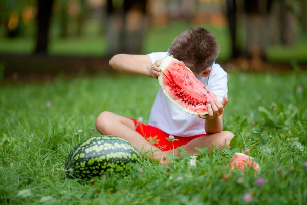Beyaz Tişörtlü Çocuk Parktaki Çimlerde Karpuz Yiyor — Stok fotoğraf