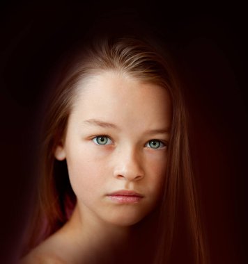 9 yaşındaki nazik, uzun saçlı bir kız. Duvara yaslanmış.