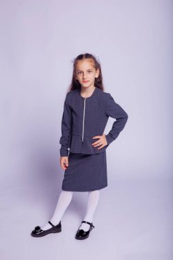 Katı okul kıyafetleri içinde açık gri arka planda bir kızın portresi.