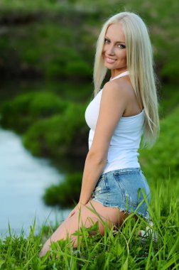 Kız bir çim bir günbatımı üzerinde oturur.