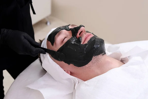 Terapia de spa para homens recebendo máscara preta facial . — Fotografia de Stock