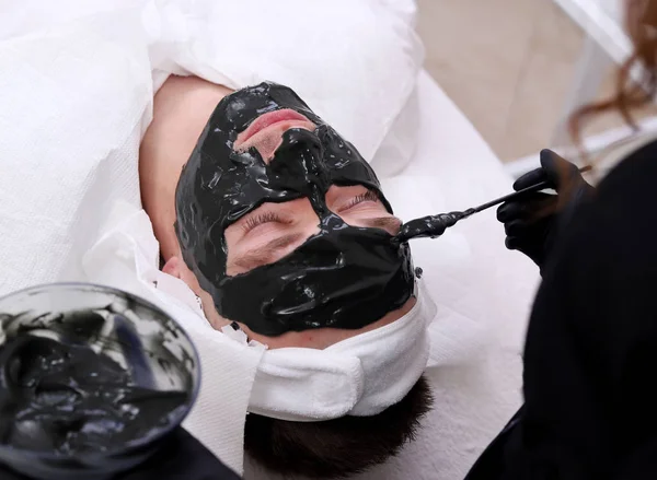 Terapii spa dla mężczyzn otrzymujących czarna maska do twarzy. — Zdjęcie stockowe