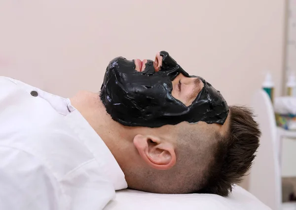 Terapia de spa para hombres que reciben mascarilla negra facial . — Foto de Stock