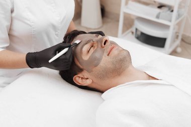 Şevval özçelik güzellik spa salonda adamın yüzündeki kozmetik maskesi uygulama.