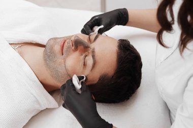 Şevval özçelik güzellik spa salonda adamın yüzündeki kozmetik maskesi uygulama.