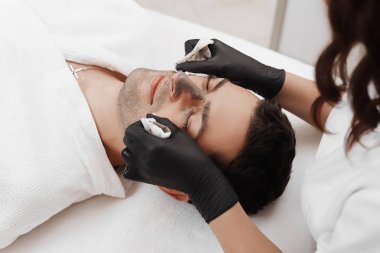 Şevval özçelik güzellik spa salonda adamın yüzündeki kozmetik maskesi uygulama.