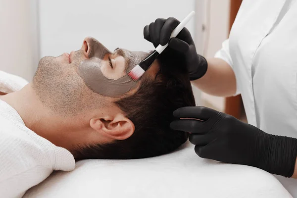 Beautician applying cosmetic mask on man's face in spa salon. — Stock Photo, Image