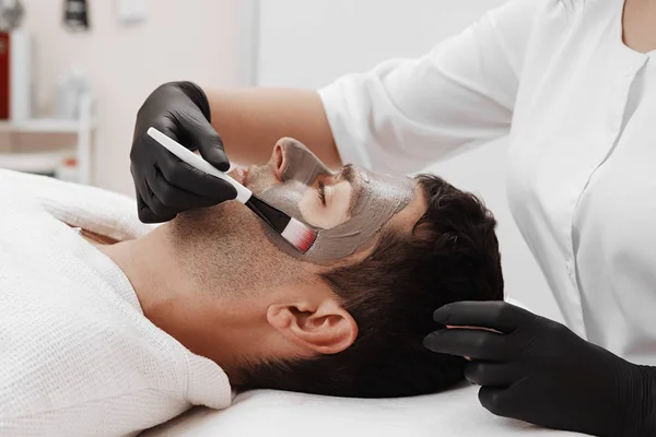 Kosmetyczka zastosowanie kosmetyczne maski na twarzy mężczyzny w salonie spa. — Zdjęcie stockowe