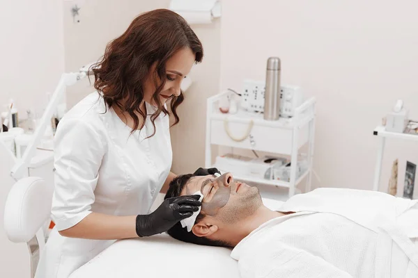 Esteticista aplicando máscara cosmética no rosto do homem no salão de spa . — Fotografia de Stock