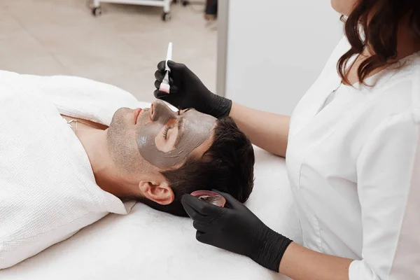 Beautician applying cosmetic mask on man's face in spa salon. — Stock Photo, Image
