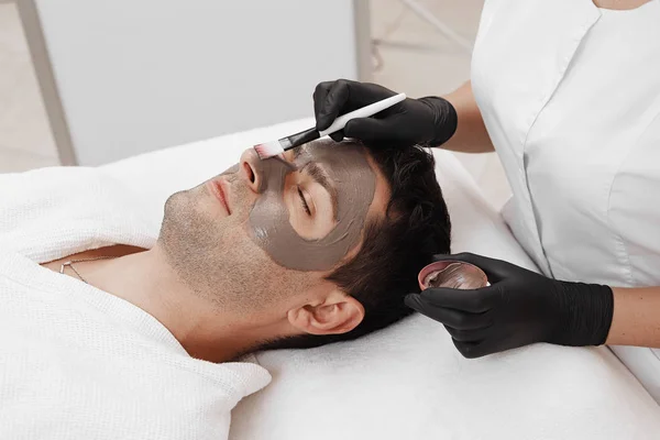 Beautician applying cosmetic mask on man's face in spa salon. — Stock Photo, Image