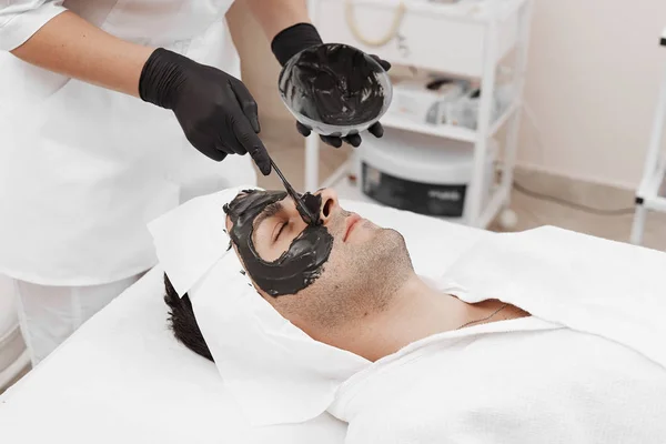 Spa therapy for men receiving facial black mask. — Stock Photo, Image