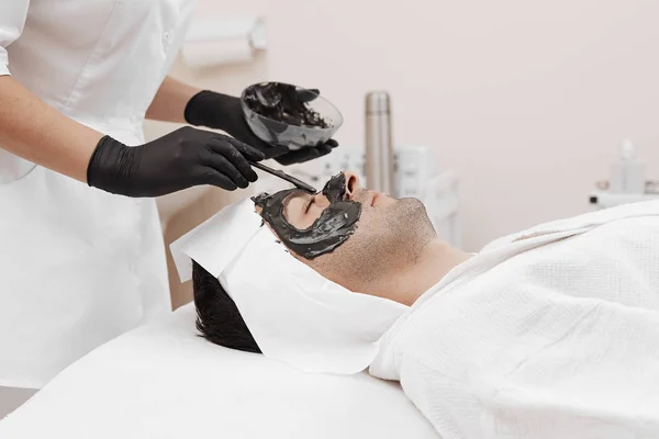 Terapii spa dla mężczyzn otrzymujących czarna maska do twarzy. — Zdjęcie stockowe