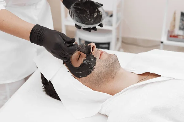 Terapia de spa para homens recebendo máscara preta facial . — Fotografia de Stock