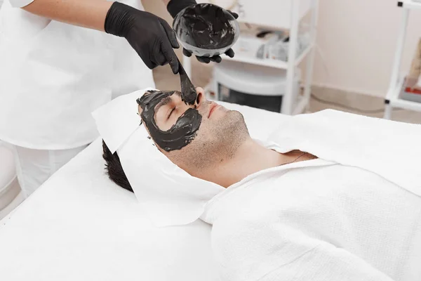 Terapia de spa para hombres que reciben mascarilla negra facial . — Foto de Stock