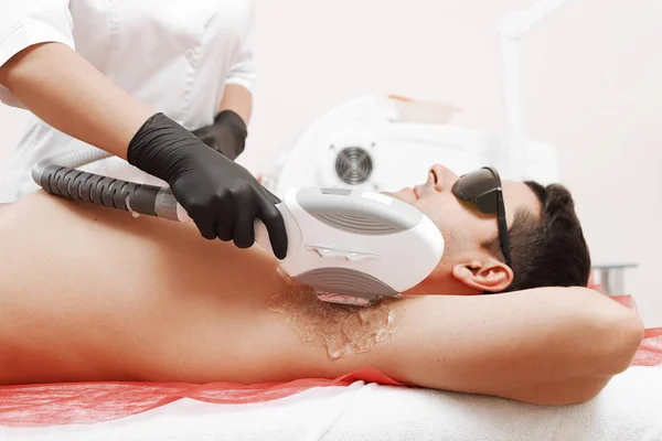 Terapeuta que da tratamiento de la acumulación del laser al hombre joven en spa — Foto de Stock