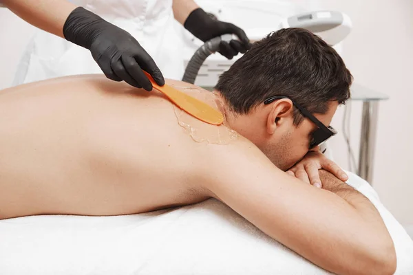 Терапевт проводит лазерную эпиляцию молодому человеку в спа — стоковое фото