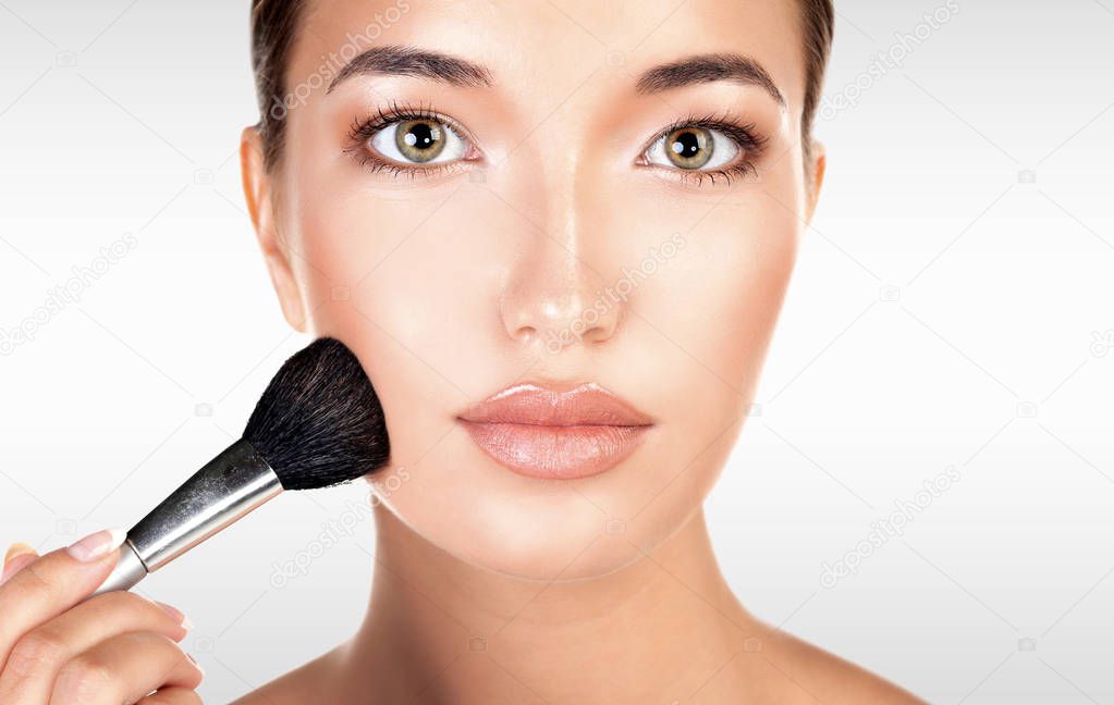 Pretty woman holds makeup brush against a grey background with copyspace