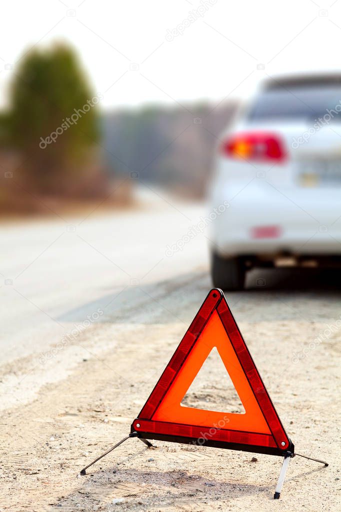 White car and a red triangle warning sign on the road