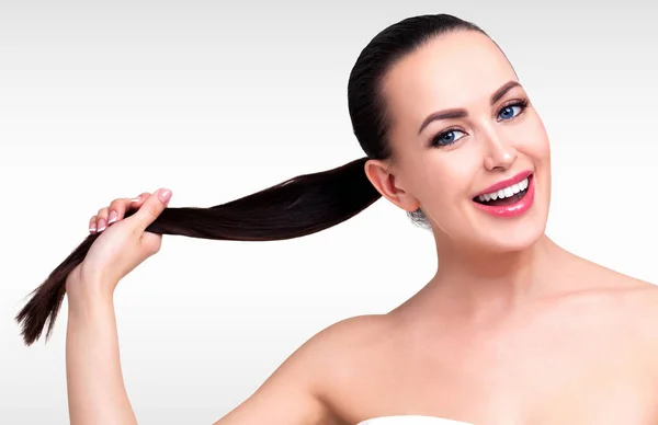 Lächelndes hübsches Mädchen mit schönen langen dunkelbraunen Haaren, grauem Hintergrund. Haut- und Haarpflege-Konzept — Stockfoto