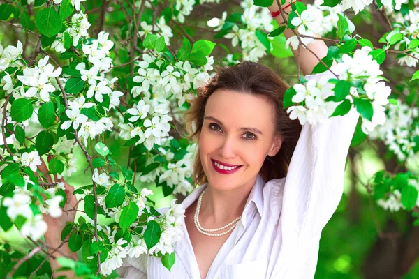Mulher bonita em camisa branca posando em árvores de maçã floridas — Fotografia de Stock