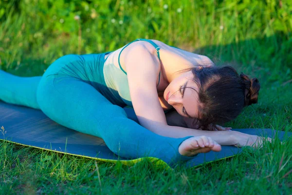 Beautiful young woman doing stretching exercise on green grass in a field or a park. — Stock Photo, Image