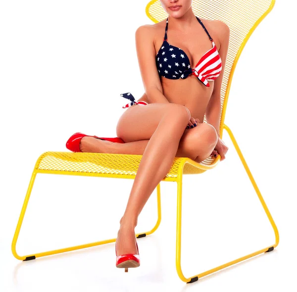 Sexy Frau im Bikini-Badeanzug sitzt auf einem gelben Sessel, weißer Hintergrund — Stockfoto