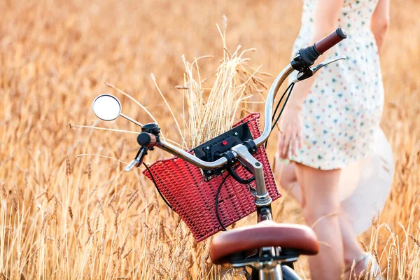 小麦の耳の間の畑に女性と自転車が立っている — ストック写真