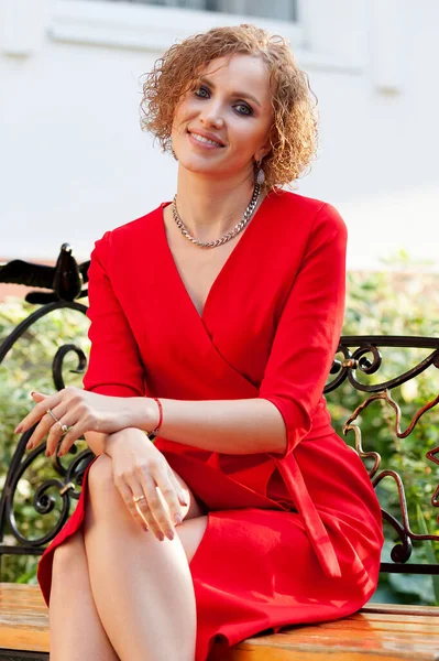 Szczęśliwa Kobieta Czerwonej Sukience Siedzi Ławce Parku Uśmiecha Się — Zdjęcie stockowe
