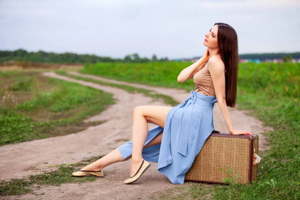 Güzel kız köy yolunda eski bir bavulun üzerinde oturuyor.