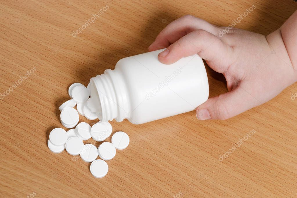 Child's hand touching overturned bottle of pills. Pills are spilled out.
