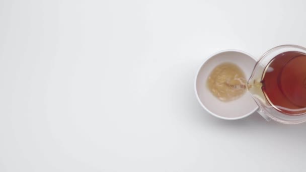 女性的手从白色的背景上的玻璃水壶倒在中国杯子里的茶 慢动作 第41部分 — 图库视频影像