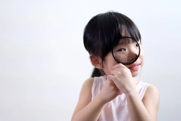 Menina criança olhando através de uma lupa no fundo branco — Fotografia de Stock
