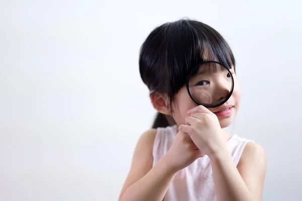 Petite fille enfant regardant à travers une loupe sur fond blanc — Photo