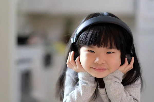 Mladá Asijská dívka se těší poslouchat hudbu na její sluchátka — Stock fotografie