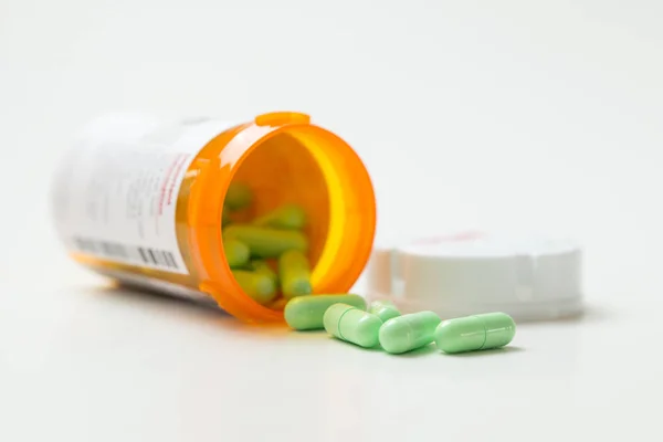 Green capsules cascading out of orange bottle — Stock Photo, Image