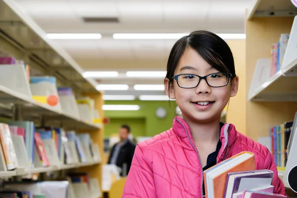 Asiatisk tonårsflicka står med böcker i biblioteket — Stockfoto